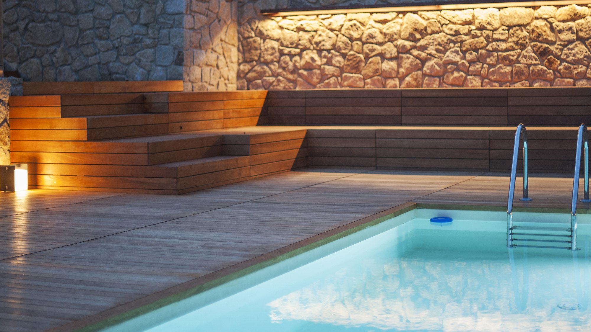 Solarium in legno con gradonata illuminata e bordo piscina, di sera
