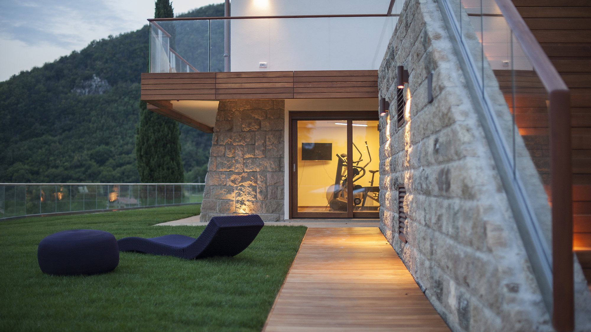 Villa in pietra con rivestimento in legno e camminamento esterno illuminato al tramonto